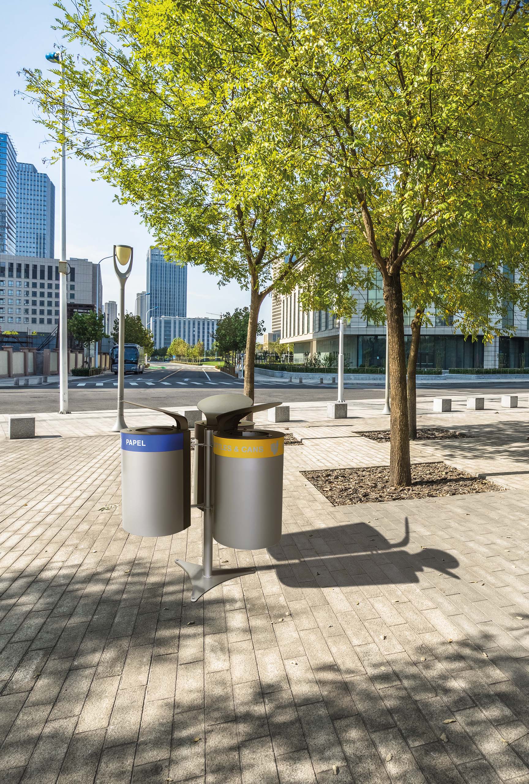 Zweigeteilter Abfall‑ und Recyclingbehälter auf einem sonnigen Stadtweg, umgeben von Bäumen und modernen Gebäuden.