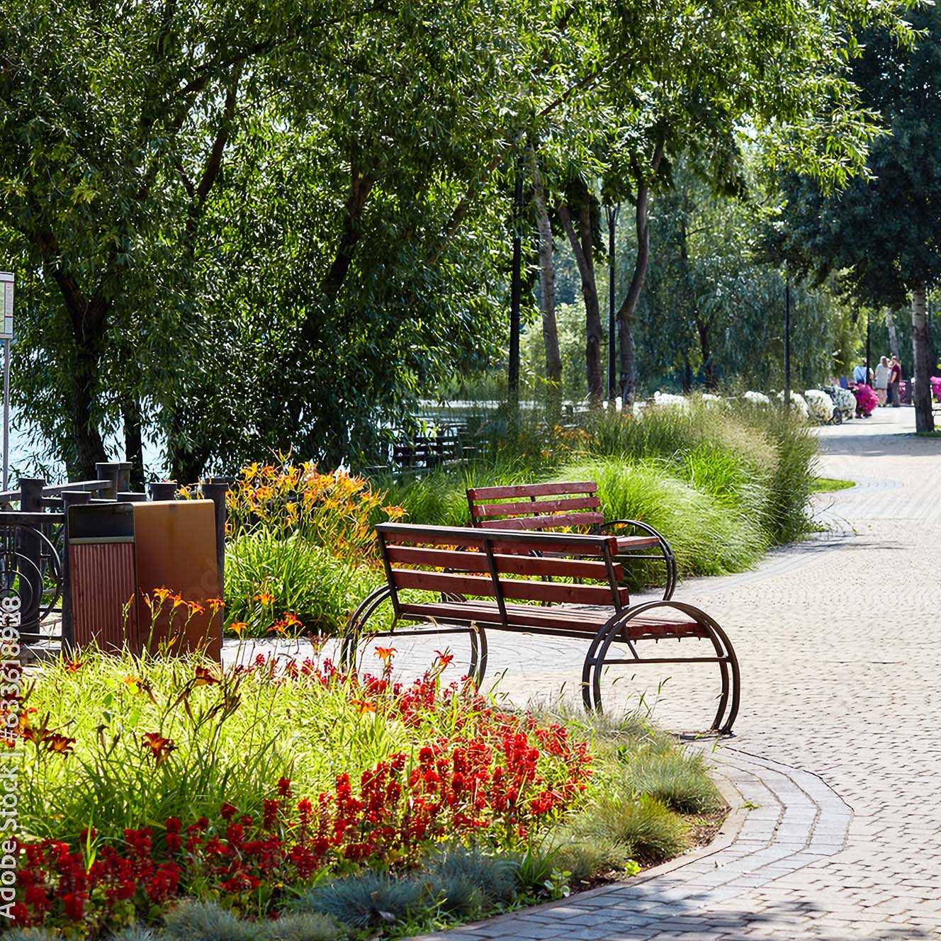 Einladende Promenade an einem Flussufer. Blühende Uferbepflanzung mit einladenden Sitzbänken und den passenden, holzvertäfelten Mülleimern.